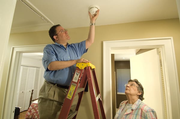 woman holding a ladder for a man installing a smoke alarm