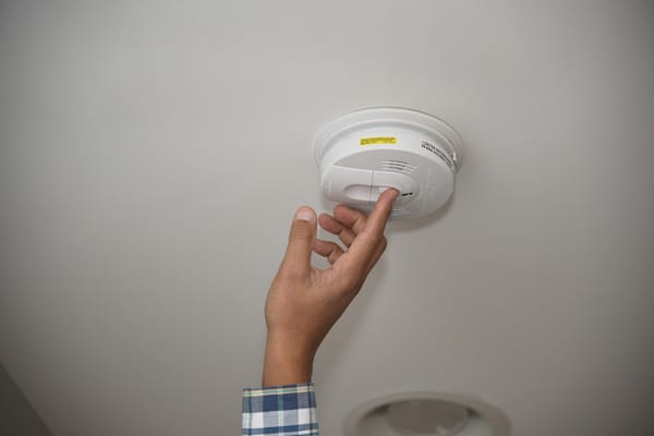hand reaching up to test a smoke alarm