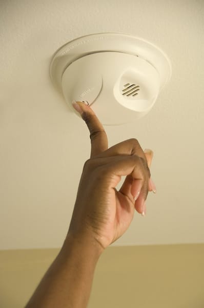 closeup of hand reaching up to test smoke alarm